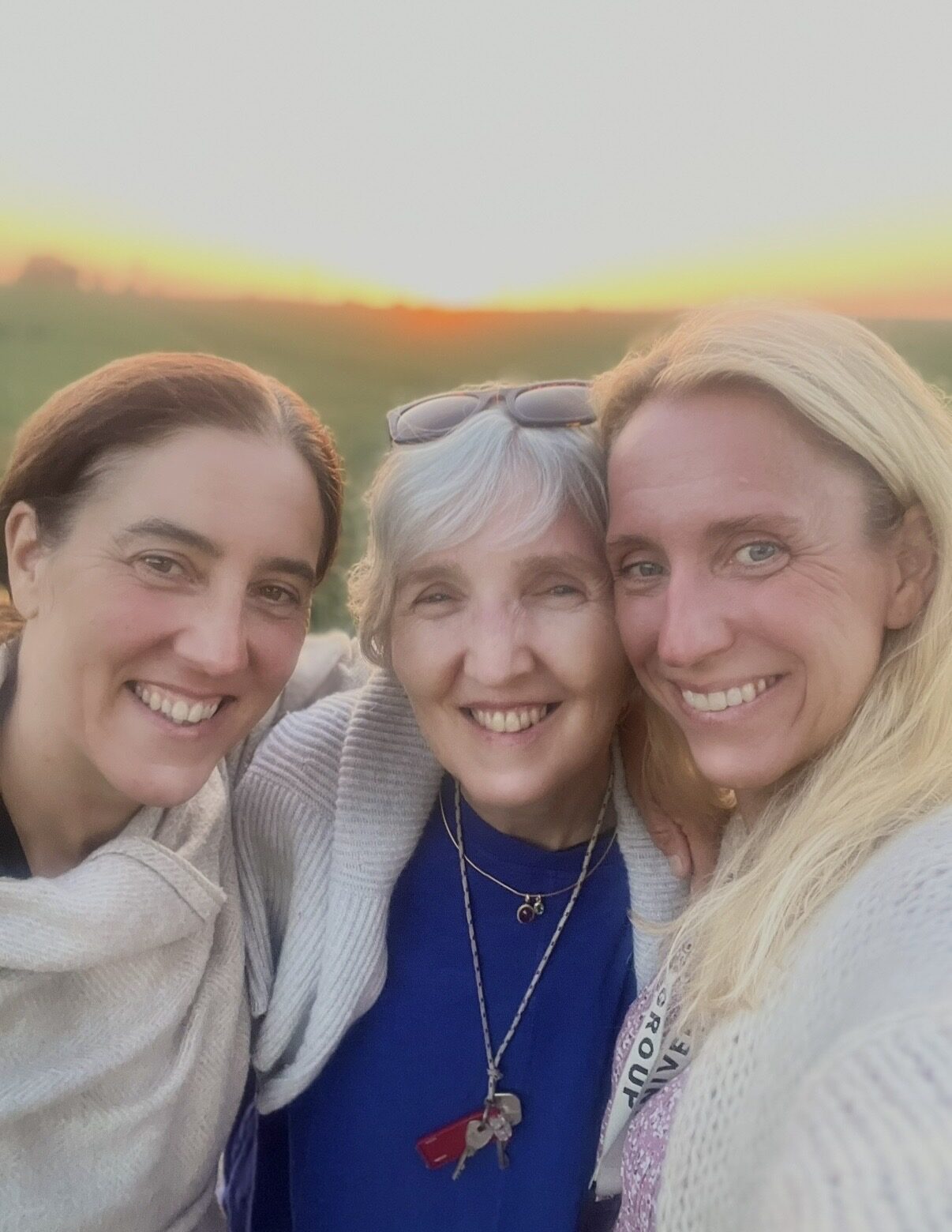 Drei Frauen dicht beieinander vor einer Wiese im Abendlicht